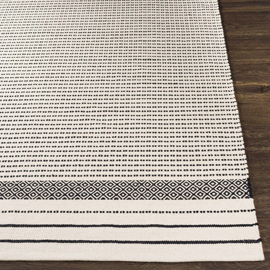 Close-up of Calumpang Area Carpet. Beige cotton rug with black stripes and Southwestern-inspired diamond border. Hand woven texture. Front