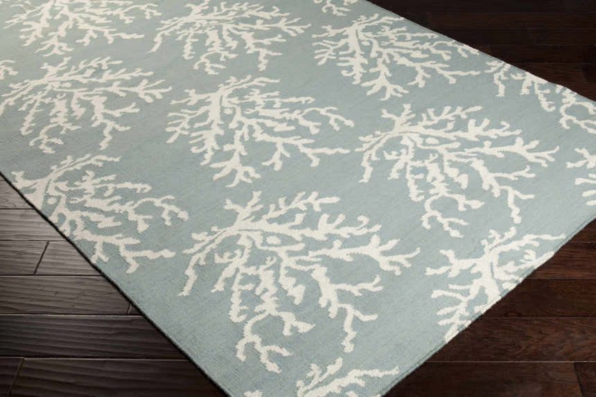 Close-up of Carversville Ice Blue Botanical Wool Rug with ivory coral pattern on dark wood floor. Corner
