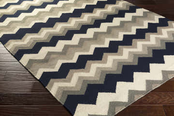 Close-up of the Cherry Area Rug. Hand-woven wool rug with a contemporary chevron pattern in charcoal, gray, ink blue, and taupe. Corner