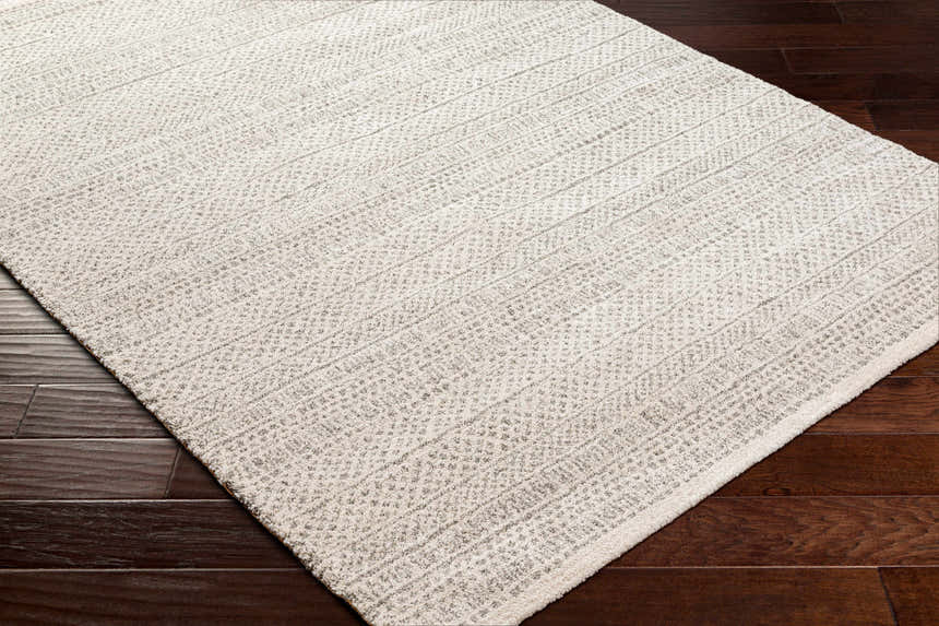 Close-up of the Cinco Luxe Rug in bone and driftwood, showing its subtle geometric pattern and soft texture on dark wood floors. Corner