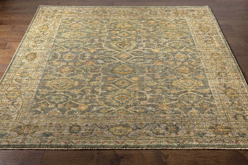 Close-up of the hand-knotted Clunes Area Rug in black, brown, sage, and yellow on a dark wood floor. Oriental rug style. Front