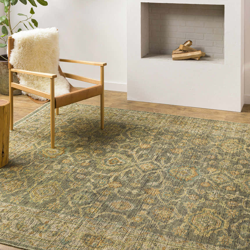 Living room scene with Clunes Area Rug in sage, yellow, and beige. A chair with a sheepskin throw sits on the rug near a fireplace. Styleshot