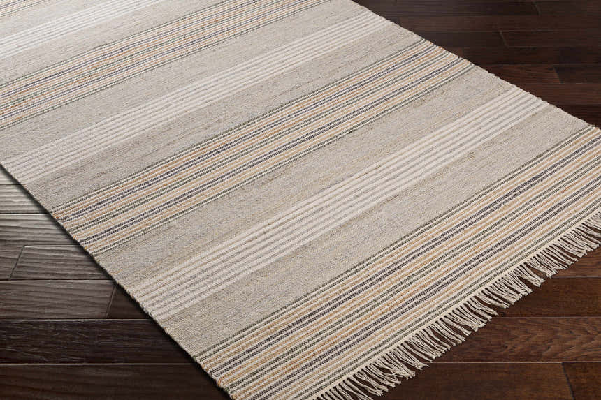 Close-up of the hand woven Calinog Area Rug. Features a striped pattern in charcoal, tan, and beige on dark wood floors. Corner