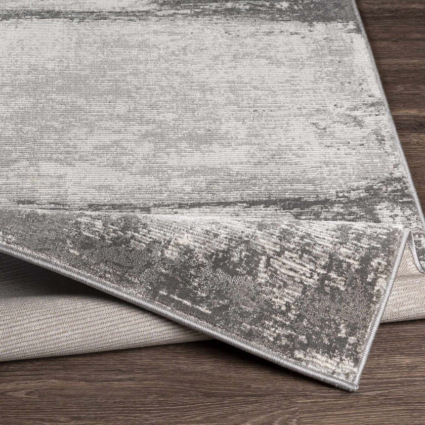 Close-up of the Coombs Area Rug, showcasing its charcoal, gray, and light gray abstract design and machine-woven texture. Fold