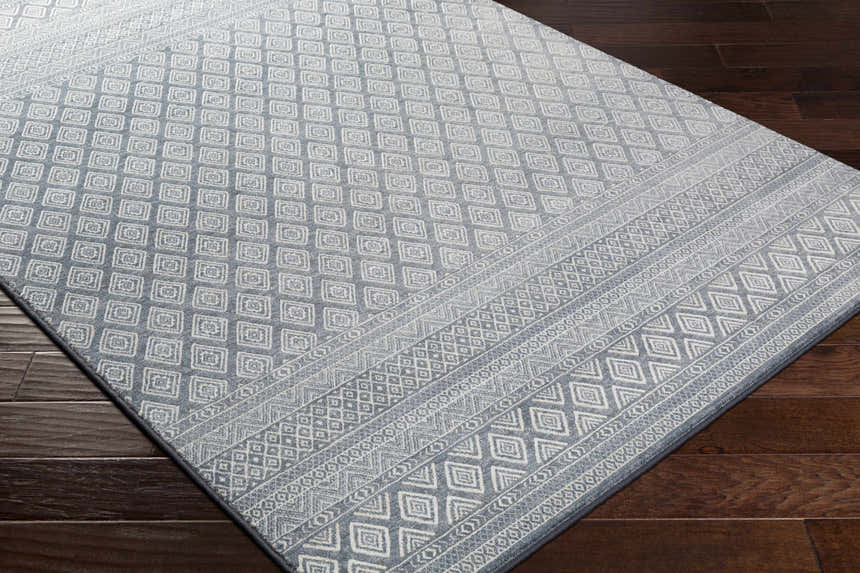 Close-up of Centertown Area Rug. Blue and ivory geometric pattern. Farmhouse style rug on dark wood floor. Corner