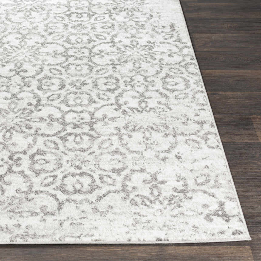 Close-up of the Cordele Area Rug. White rug with a gray traditional floral pattern on dark wood flooring. Front