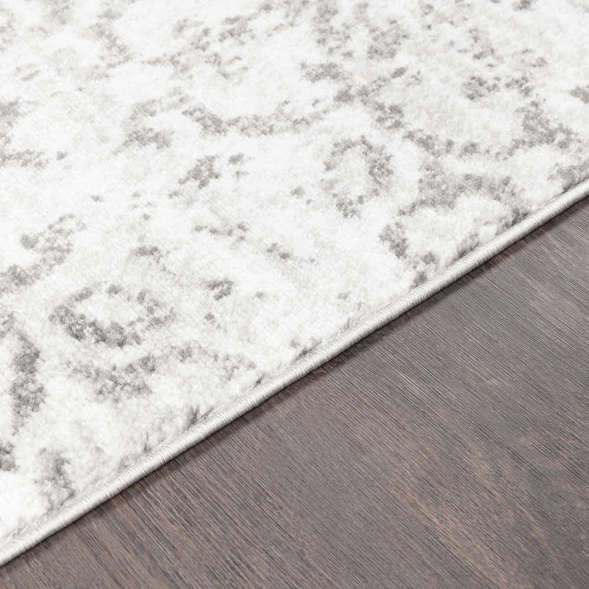 Close-up of the Cordele Area Rug showing its white and gray traditional pattern and soft texture on dark wood floor. Texture