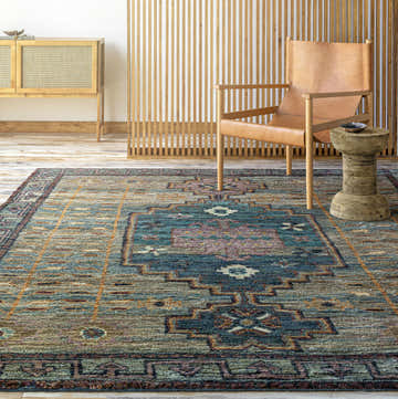 Living room scene with a Cowell Jute Area Rug in burnt orange, pink, blue, and green tones. Bohemian style with a leather chair. Roomscene-Rectangle