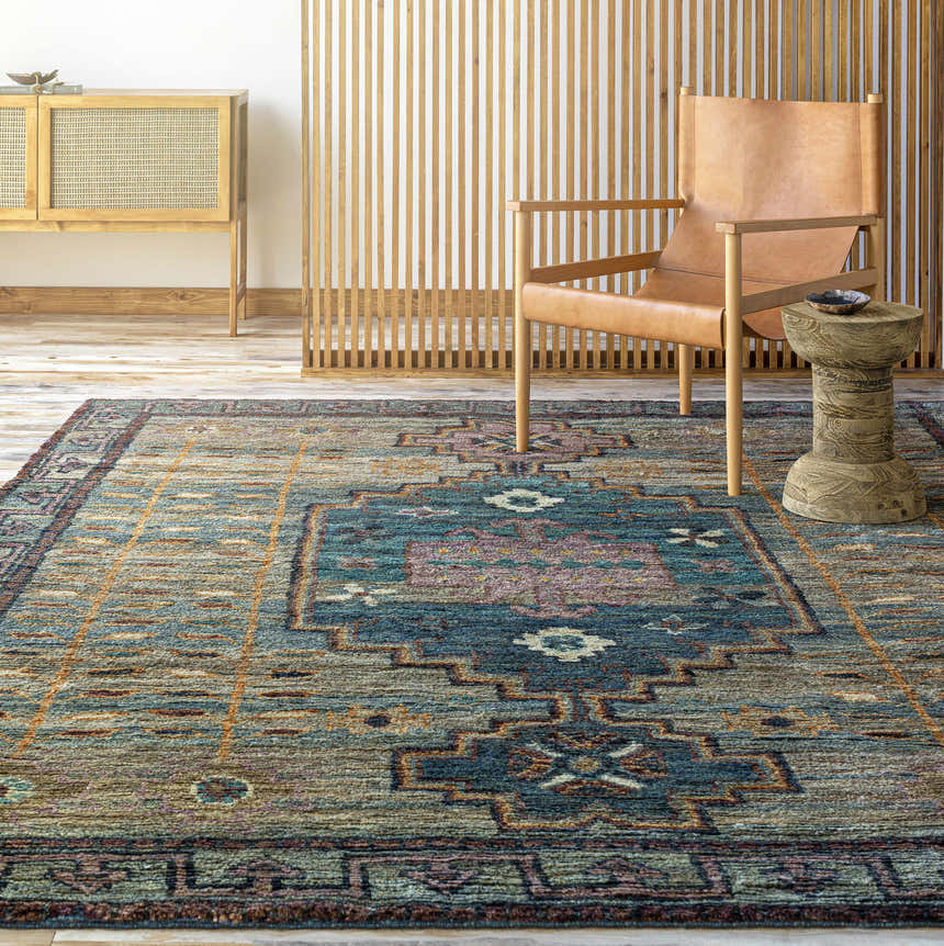 Living room scene with a Cowell Jute Area Rug in burnt orange, pink, blue, and green tones. Bohemian style with a leather chair. Roomscene-Rectangle