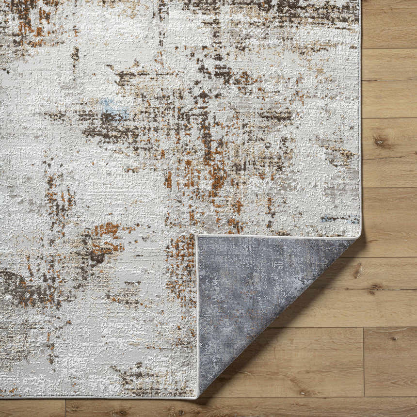 Close-up of the Utcha Area Rug, clearance item. Features dark brown, denim, mustard, and taupe abstract pattern. Fold