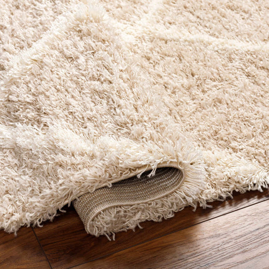 Close-up of the plush texture and backing of the ivory Dacre Shag Area Rug on a wood floor. Fold