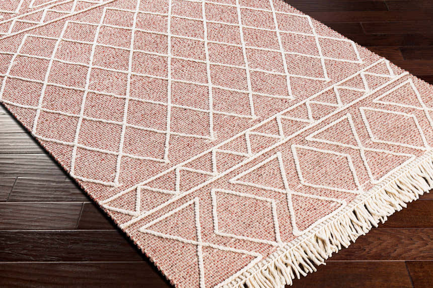 Close-up of the hand woven Dacudao Area Rug. Burgundy and cream wool rug with geometric diamond pattern and fringe. Corner