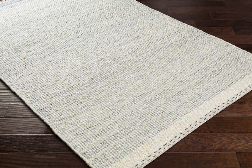 Close-up of Dalaoig Flat Woven Wool Rug. Charcoal, cream, and gray tones. Hand woven texture on dark wood floor. Corner
