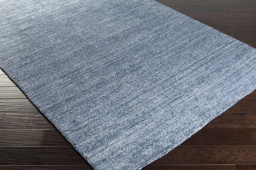 Close-up of the blue Davy Viscose Area Rug showing its subtle striped pattern and soft texture on dark hardwood flooring. Corner
