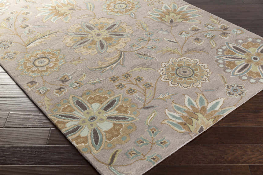 Close-up of the hand-tufted Denio Area Rug. Floral pattern in brown, sage, taupe, and sky blue on a light brown wool rug. Corner
