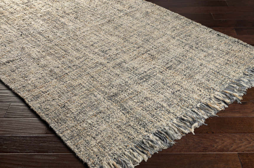 Close up of the hand woven Edgely Area Rug showing texture and fringe detail. Colors are black, gray, light beige, and tan. Corner