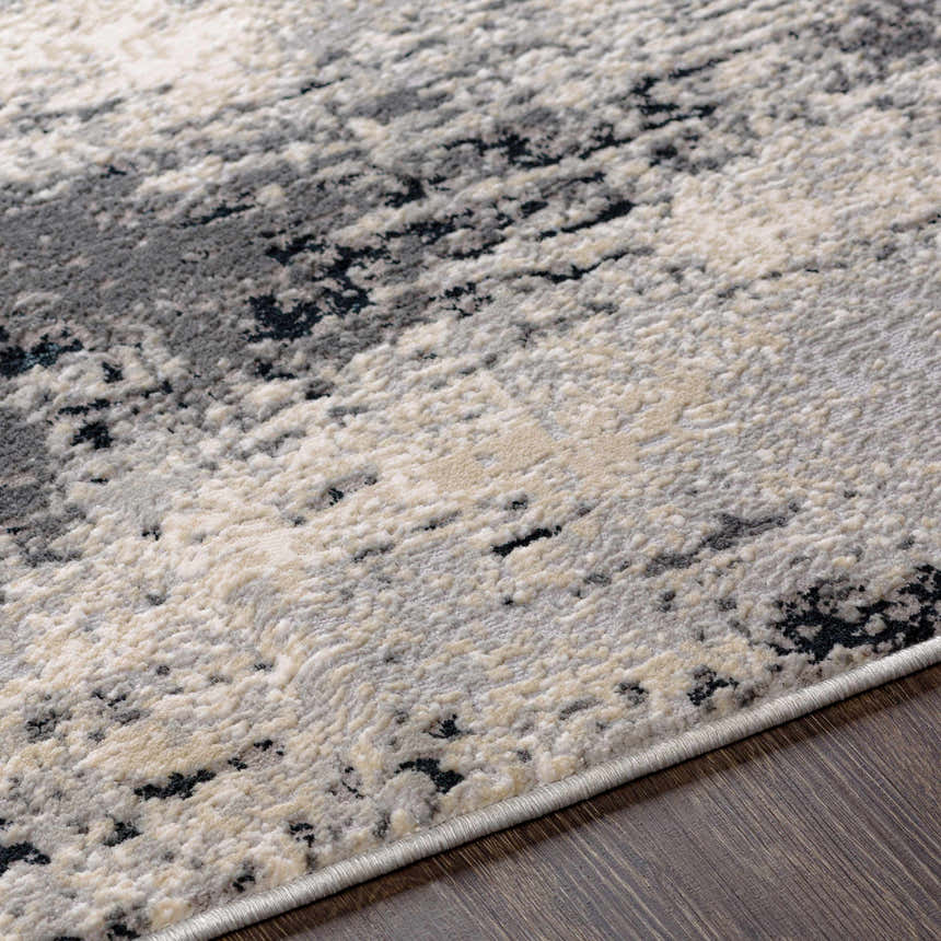 Close-up of the Dumangas Area Rug, showcasing its contemporary black, charcoal, cream, and gray abstract pattern and soft texture. Texture