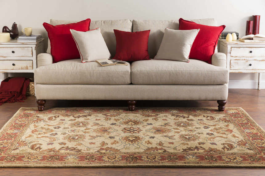 Living room scene with a Cherryfield Brown & Rust Wool Rug, beige sofa with red pillows, and white side tables. Roomscene-Rectangle