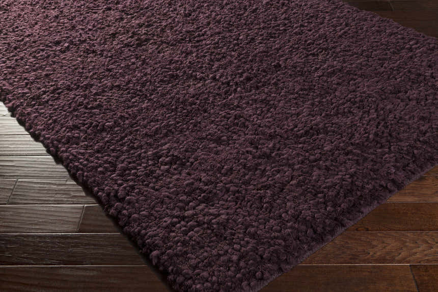 Close-up of the plum Duncanville Area Carpet showing its hand woven texture on dark wood flooring. Corner