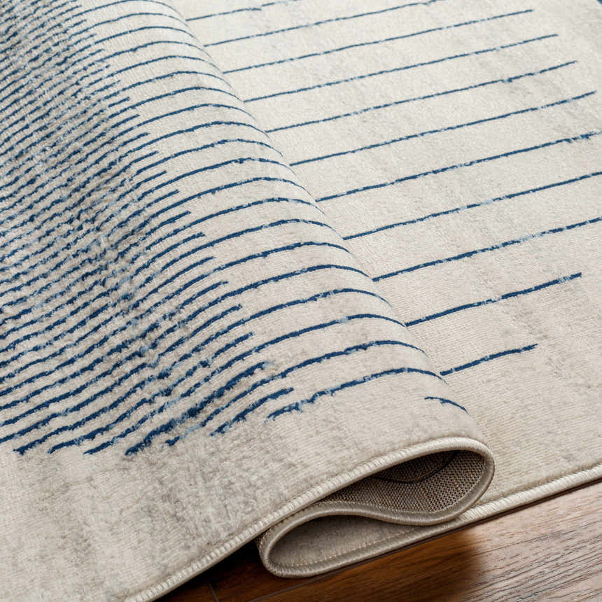 Close-up of the Duri Area Rug. Features a geometric pattern with admiral blue lines on a natural gray background. Fold