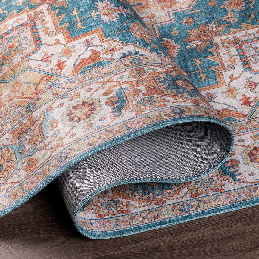 Close-up of rolled Eglinton Area Carpet. Oriental design with burnt orange, dark blue, and beige tones. Machine woven polyester rug. Fold