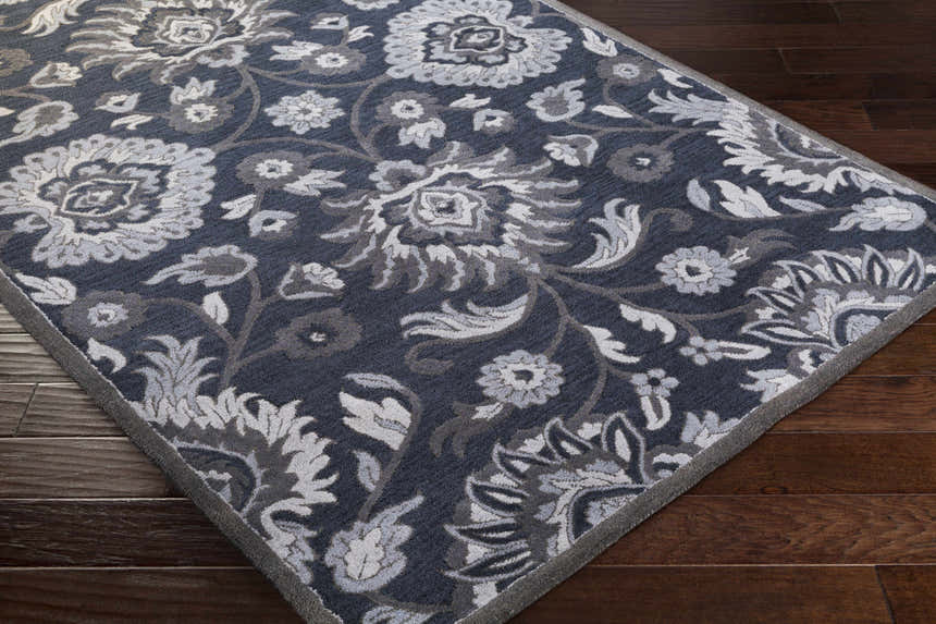 Close-up of the Conesus Hand Tufted Blue Area Rug showing its floral pattern and texture on dark wood flooring. Corner