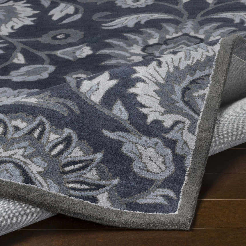Close-up of the Conesus Hand Tufted Blue Area Rug showing its floral pattern, wool texture, and charcoal, denim, and slate blue colors. Fold