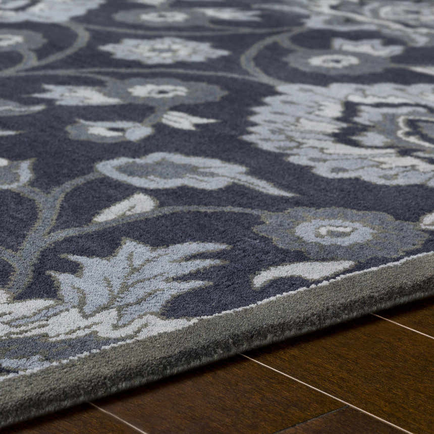 Close up of the Conesus Hand Tufted Blue Area Rug showing its floral pattern, wool texture, and charcoal, denim, and slate blue colors. Texture
