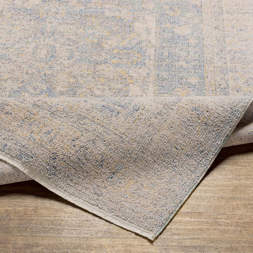 Close-up of the Tusa Blue Area Rug showing its traditional pattern, light blue, ivory, and gray colors, and soft texture. Fold