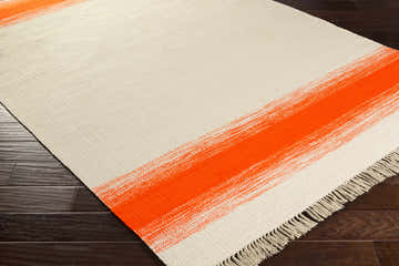 Close-up of the hand-woven Farsley Area Rug. Features a cream background with bold orange brushstroke stripes and fringe. Corner