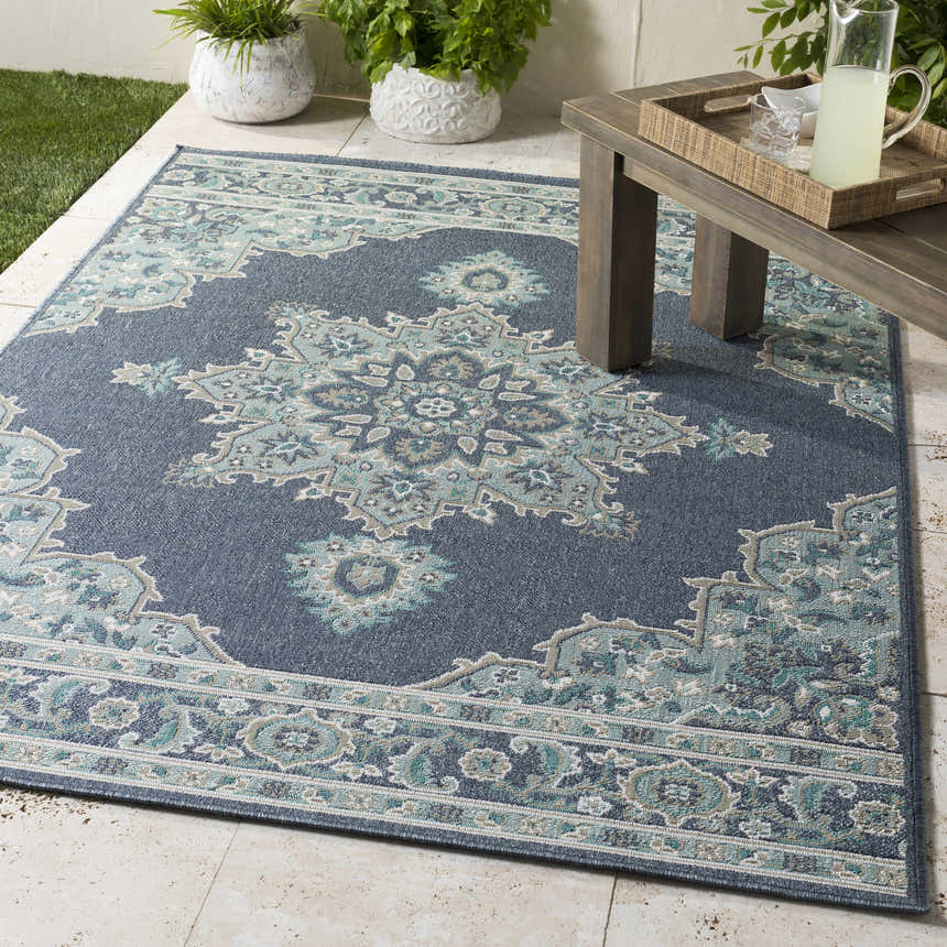Outdoor patio scene with the navy Ferron Area Rug, a wood table, and potted plants. Roomscene-Rectangle