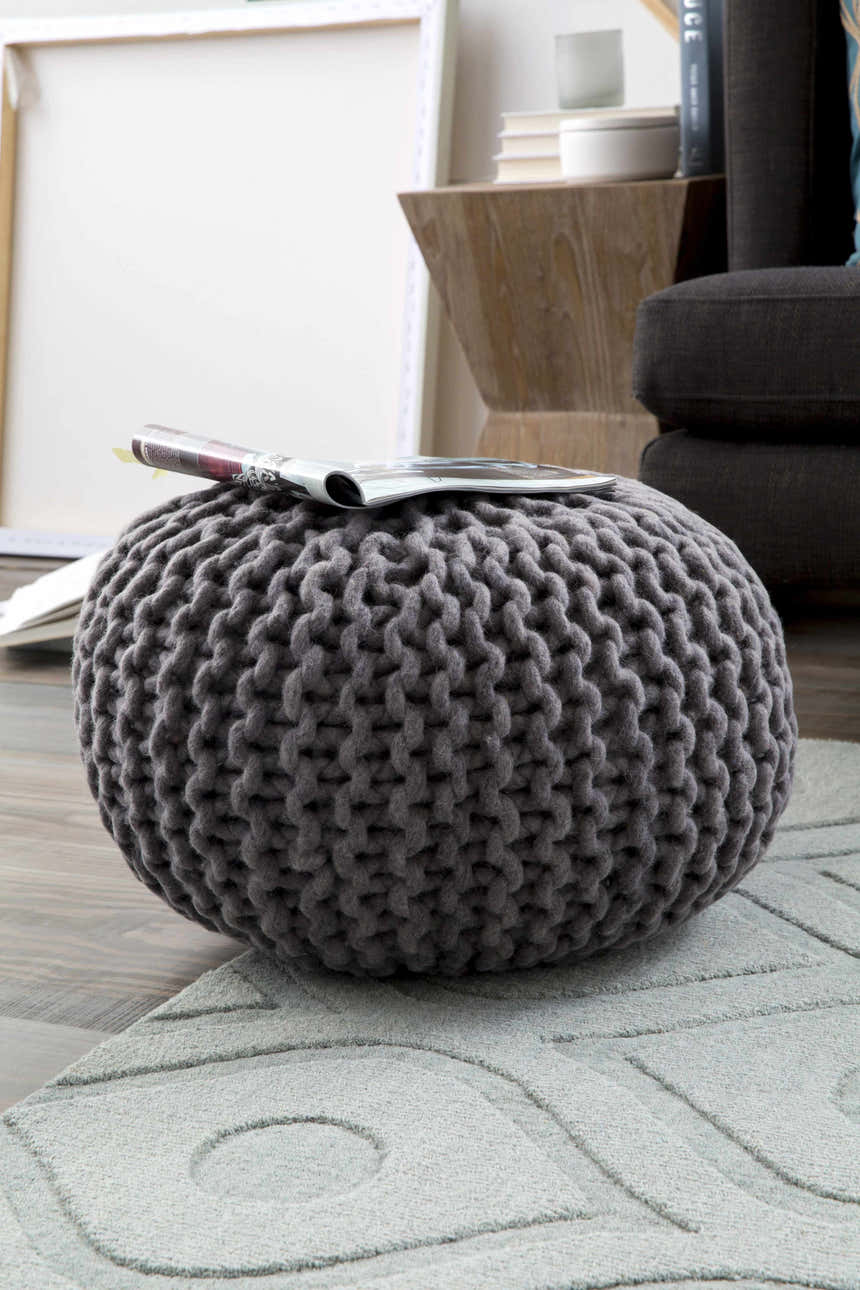 Living room scene with a light gray Welaka Eye Pattern Wool Rug and a gray knitted pouf. Styleshot