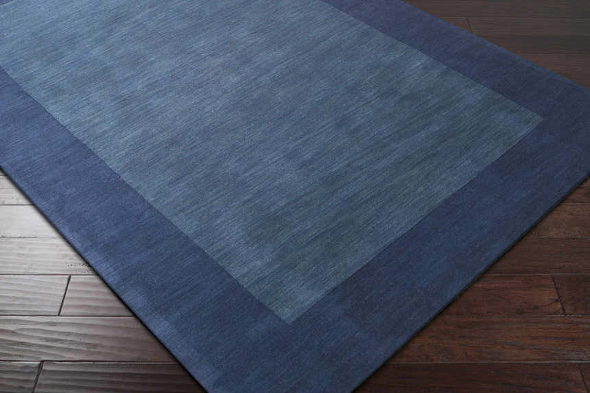 Close-up of a Bordered Solid Ink Blue Wool Rug showing texture and border detail on dark wood flooring. Corner