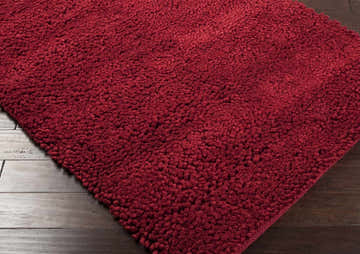 Close-up of the Frederika Solid Dark Red Wool Shag Rug showing its plush texture and rich color on dark wood flooring. Corner