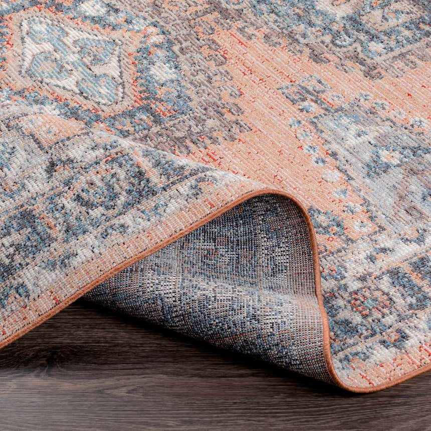 Close up of the Fullarton Performance Rug showing beige, blue, and brick red colors with a traditional pattern. Fold