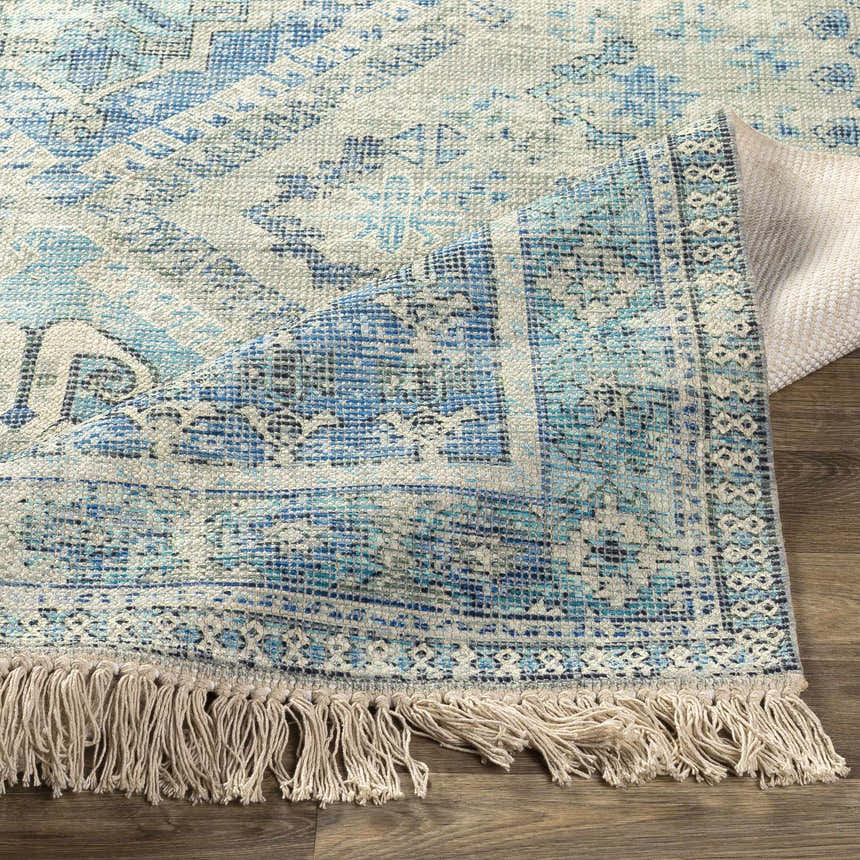 Close-up of the hand-woven Galgate Area Rug. Aqua, teal, and white farmhouse-style rug with fringe detail. Fold