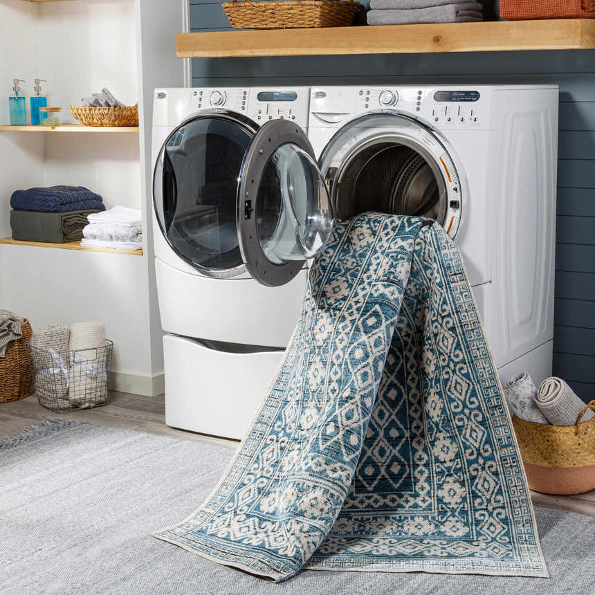 Laundry room scene with Gandy Washable Area Rug partially inside a washing machine. Blue and cream rug. Washing-Machine