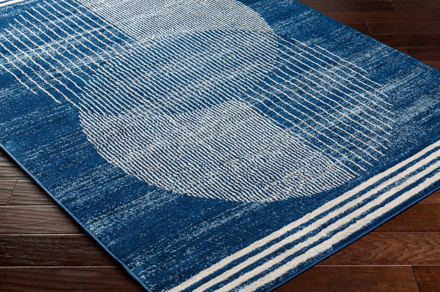 Close-up of the Gent Area Rug. Harbor blue rug with a geometric pattern of white lines and a distressed texture. Corner