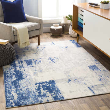 Living room scene with Gerton Area Rug in denim, gray, and ivory. Features armchair, ottoman, and mid-century modern cabinet. Roomscene-Rectangle