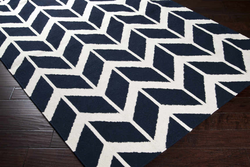 Close-up of the Gilchrist Area Carpet. Ink blue and light beige geometric pattern on a hand woven wool rug. Corner