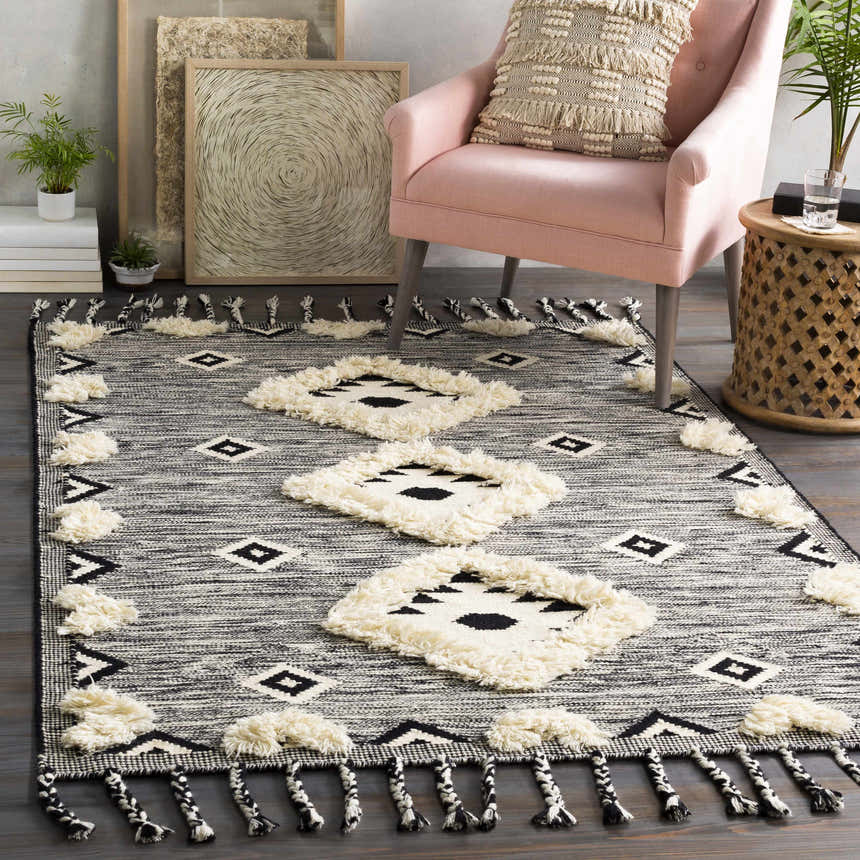 Bohemian living room scene with a Gardner Cream on Gray Wool Tassel Rug, pink chair, and eclectic decor. Roomscene-Rectangle