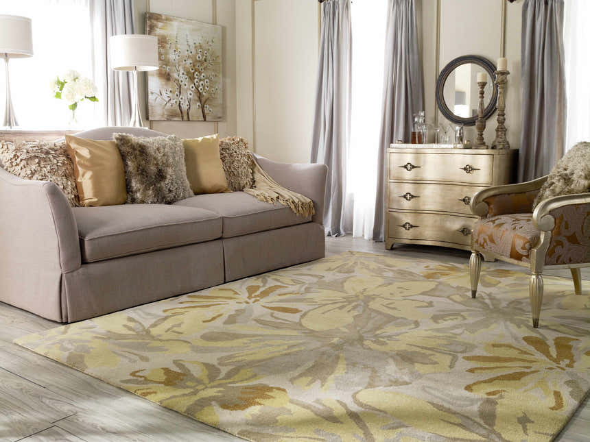 Living room scene with floral Grindstone Area Rug in light gray, olive, tan, and wheat tones. Sofa, chair, and dresser are visible. Roomscene-Rectangle
