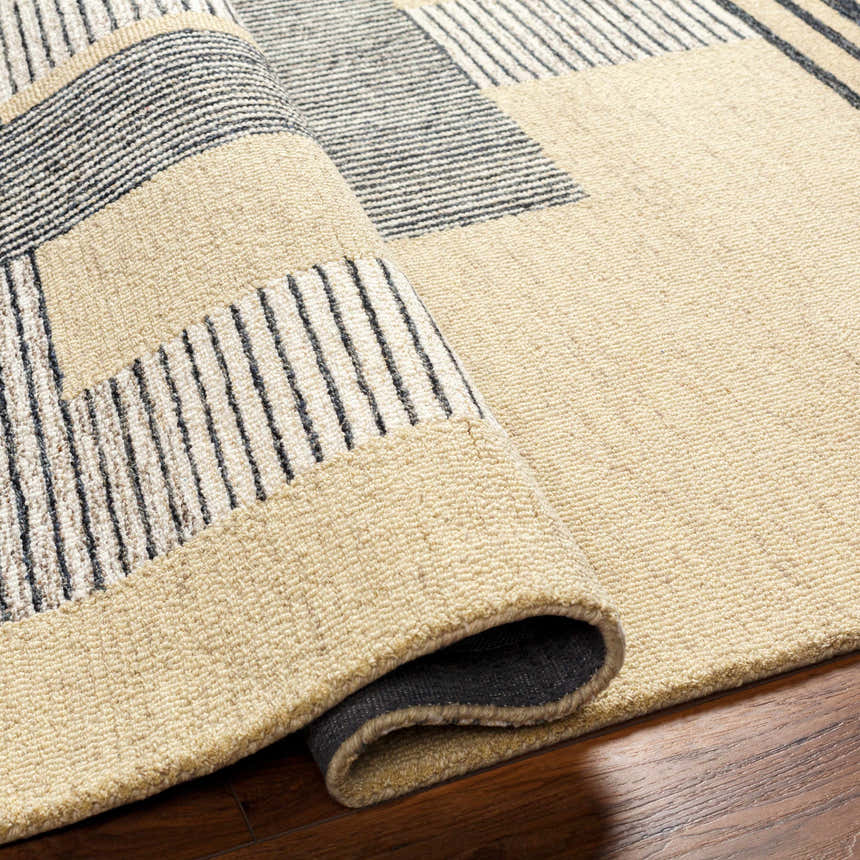 Close-up of the hand-tufted Guta Area Rug. Beige wool rug with a black striped geometric pattern and textured pile. Fold