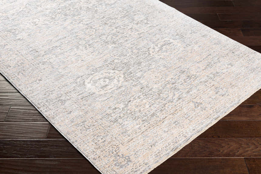 Close-up of the Guiwanon Area Rug. Cream, gray, and peach tones with a traditional pattern on a dark wood floor. Corner