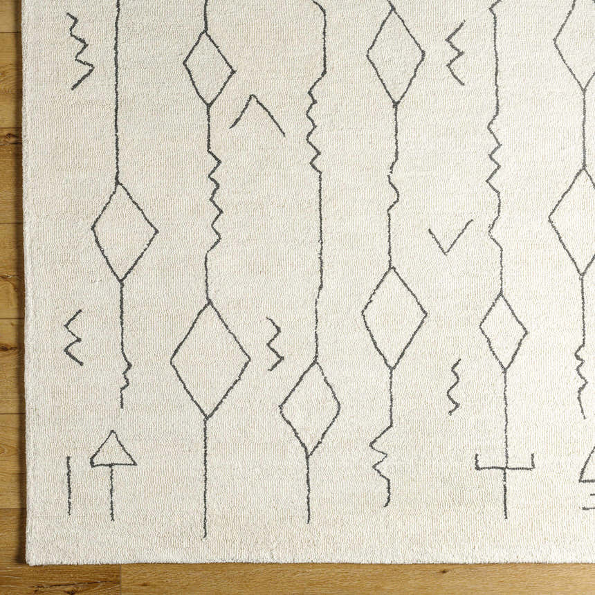Close up of the hand tufted Hanny Area Rug. Beige wool rug with black geometric shapes. Corner