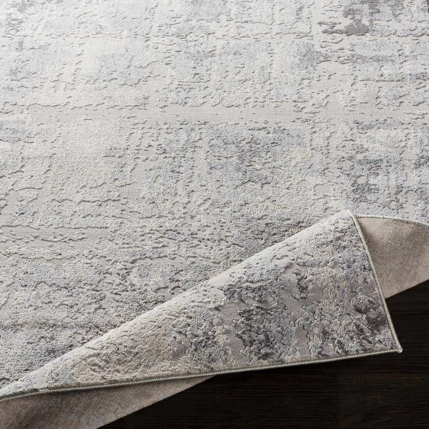 Close-up of Hardeeville Area Rug: a textured, abstract pattern in shades of gray and white on dark wood. Fold