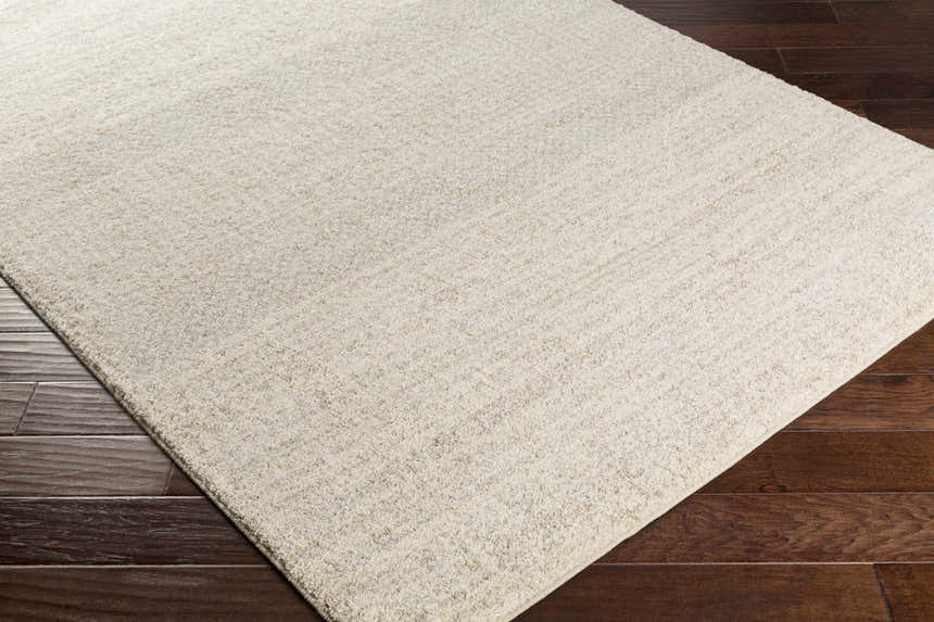 Close-up of the Harpursville Area Rug. Light gray rug with a subtle texture on dark wood flooring. Corner
