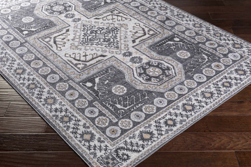 Close-up of the Harrah Gray Cross Rug showing its charcoal, cream, and gray traditional pattern and machine-woven texture. Corner