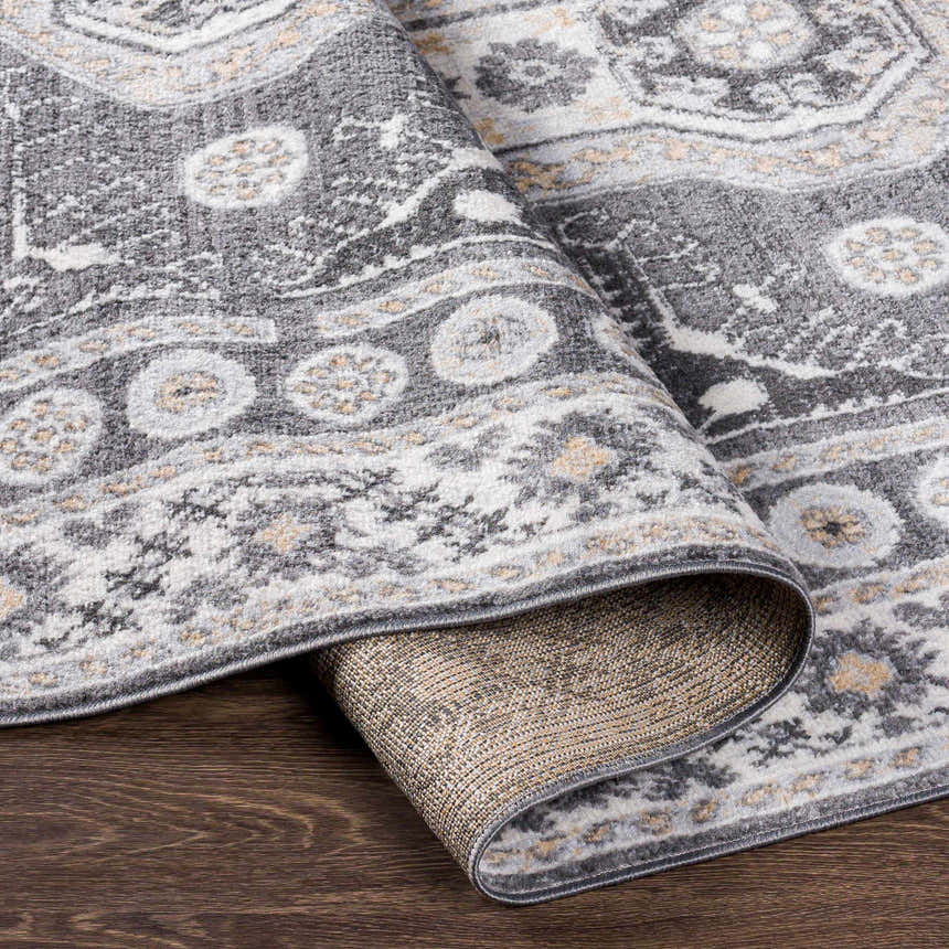 Close-up of the Harrah Gray Cross Rug showing its charcoal, cream, and gray traditional pattern and polypropylene texture. Fold
