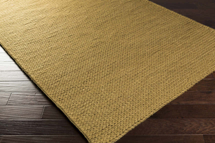 Close-up of the light brown Hensler Area Carpet showing its hand woven texture on dark wood floors. Corner